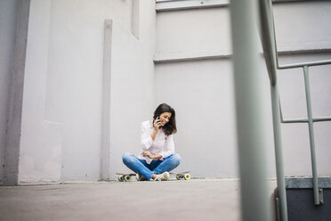 Lächelnde junge Frau am Telefon auf einem Skateboard sitzend - MOEF00485