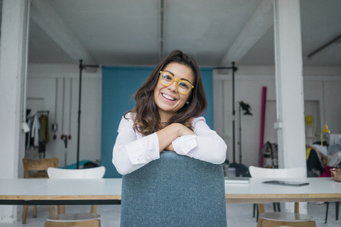 Porträt einer lachenden jungen Frau mit Brille, die in einem Atelier sitzt, lizenzfreies Stockfoto