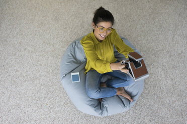 Smiling woman sitting on bean bag taking selfie with instant camera, top view - MOEF00501