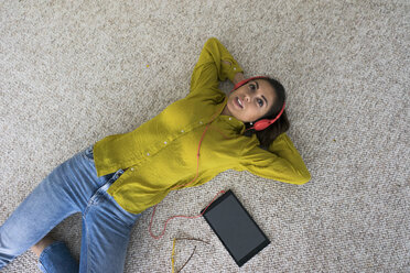 Portrait of young woman lying on the floor with headphones and tablet listening music, top view - MOEF00507