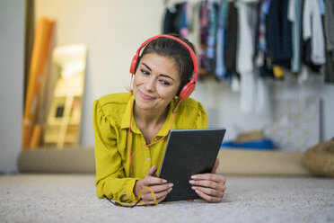 Portrait of smiling young woman lying on the floor using headphones and tablet - MOEF00509