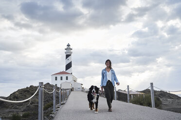 Spain, Menorca, Bernese mountain dog walking together with his owner outdoors at lighthouse - IGGF00289