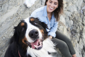 Happy bernese mountain dog looking at camera, his owner smiles next to him - IGGF00291