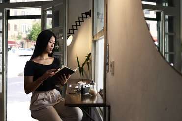 Hübsche asiatische Brünette liest ein Buch in einem Café neben dem Fenster - IGGF00297