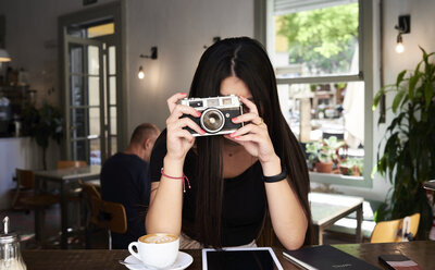 Brünettes Mädchen, das in einem Café ein Foto mit ihrer Filmkamera macht - IGGF00299