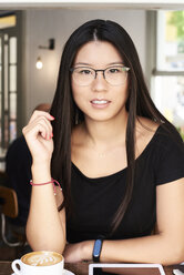 Porträt einer asiatischen jungen Frau mit Blick auf die Kamera in einem Café - IGGF00301