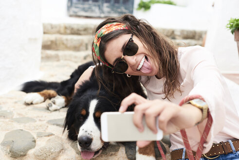 Brünettes Mädchen macht Selfie, müder Berner Sennenhund liegt auf dem Boden - IGGF00310