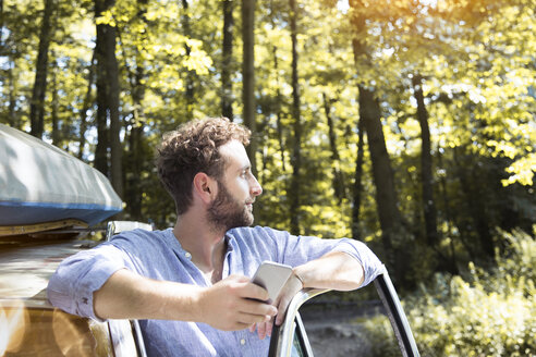 Junger Mann mit Handy am Auto im Wald - FKF02791