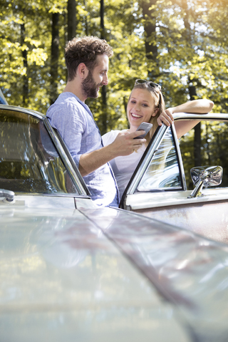 Smiling young couple with cell phone at car in forest stock photo