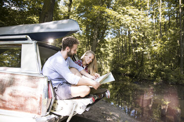 Smiling young couple with map and canoe in car at a brook - FKF02795