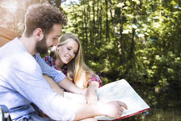Smiling young couple reading map at a brook - FKF02796