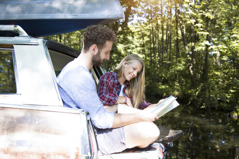 Smiling young couple with map and canoe in car at a brook - FKF02797