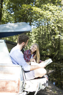 Smiling young couple with map and canoe in car at a brook - FKF02798