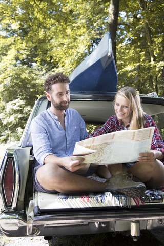 Lächelndes junges Paar mit Karte und Kanu im Auto an einem Bach, lizenzfreies Stockfoto