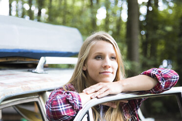 Smiling young woman at car in forest - FKF02802