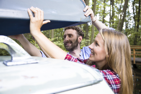 Lächelndes junges Paar nimmt Kanu vom Autodach, lizenzfreies Stockfoto