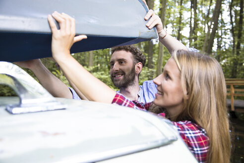 Smiling young couple taking canoe from car roof - FKF02803