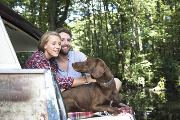 Lächelndes junges Paar mit Hund im Auto sitzend an einem Bach im Wald - FKF02807