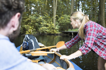 Young woman pulling canoe on a forest brook with man inside - FKF02810