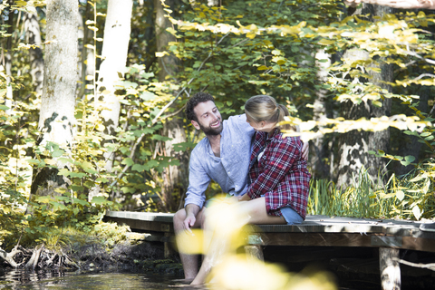 Young couple sitting on a bridge in forest with feet in water stock photo