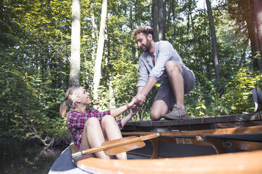 Smiling young man helping girlfriend getting out of a canoe in a forest brook - FKF02814