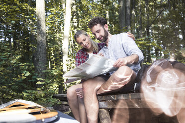 Junges Paar mit Karte und Kanu auf einem Steg an einem Waldbach sitzend - FKF02815