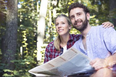 Lächelndes junges Paar mit Karte in einem Wald - FKF02816