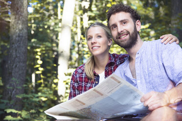 Smiling young couple with map in a forest - FKF02816