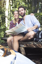 Young couple with map and canoe sitting on a jetty at a forest brook - FKF02817