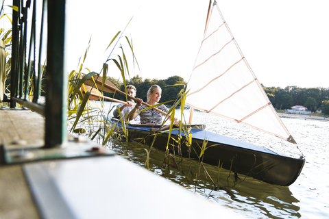 Junges Paar genießt einen Ausflug in einem Kanu mit Segel auf einem See, lizenzfreies Stockfoto
