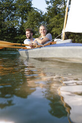 Young couple enjoying a trip in a canoe with sail on a lake - FKF02827
