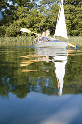 Young couple enjoying a trip in a canoe with sail on a lake - FKF02828