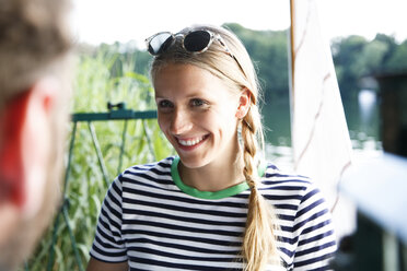 Young woman smiling at man at a lake next to sailing boat - FKF02836