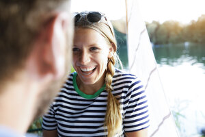 Junge Frau lacht einen Mann am See neben einem Segelboot an - FKF02837