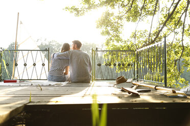 Young couple sitting on a jetty next to sailing boat - FKF02839