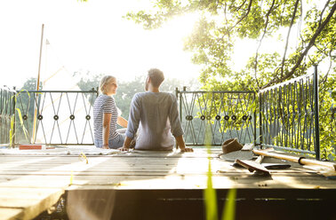 Young couple sitting on a jetty next to sailing boat - FKF02840