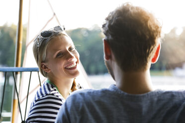Junge Frau lacht einen Mann am See neben einem Segelboot an - FKF02841