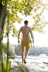 Young man with surfboard walking on a jetty at a lake - FKF02842
