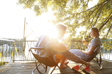 Young couple sitting on a jetty at a lake eating watermelon - FKF02844