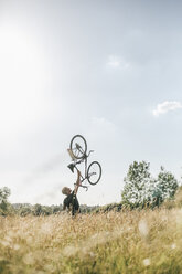 Junger Mann hebt sein Fahrrad hoch - GUSF00270