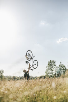 Junger Mann hebt sein Fahrrad hoch - GUSF00270