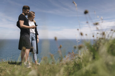 Young couple at the sea looking at smartphone - GUSF00275