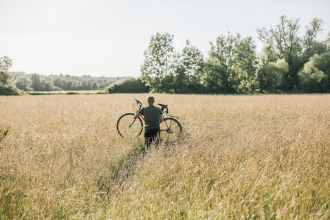 Junger Mann trägt sein Fahrrad, Feld, lizenzfreies Stockfoto