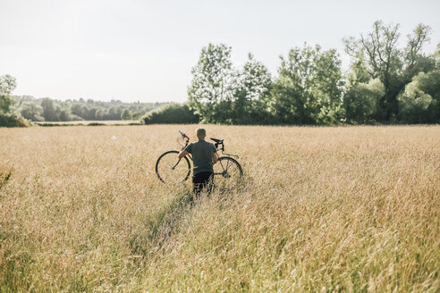 Junger Mann trägt sein Fahrrad, Feld - GUSF00283