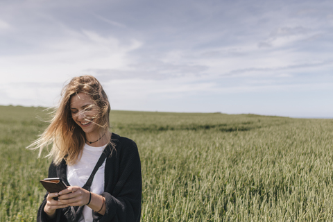Junge Frau mit Smartphone, stehend im Feld, lizenzfreies Stockfoto