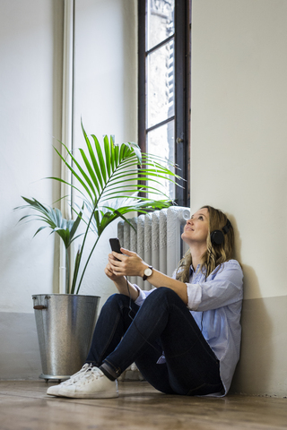 Smiling woman sitting on the floor listening to music at home stock photo