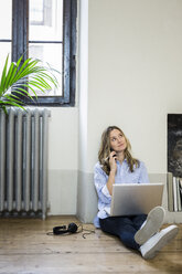Woman sitting on the floor at home using cell phone and laptop - GIOF03603