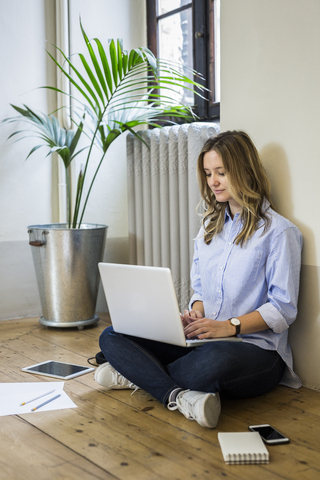 Frau sitzt zu Hause auf dem Boden und benutzt einen Laptop, lizenzfreies Stockfoto