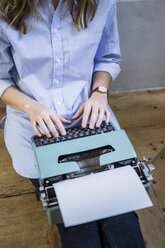 Nahaufnahme einer Frau, die auf dem Boden sitzt und eine Schreibmaschine benutzt - GIOF03606