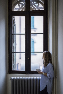 Frau mit einer Tasse Kaffee zu Hause und Blick aus dem Fenster - GIOF03608